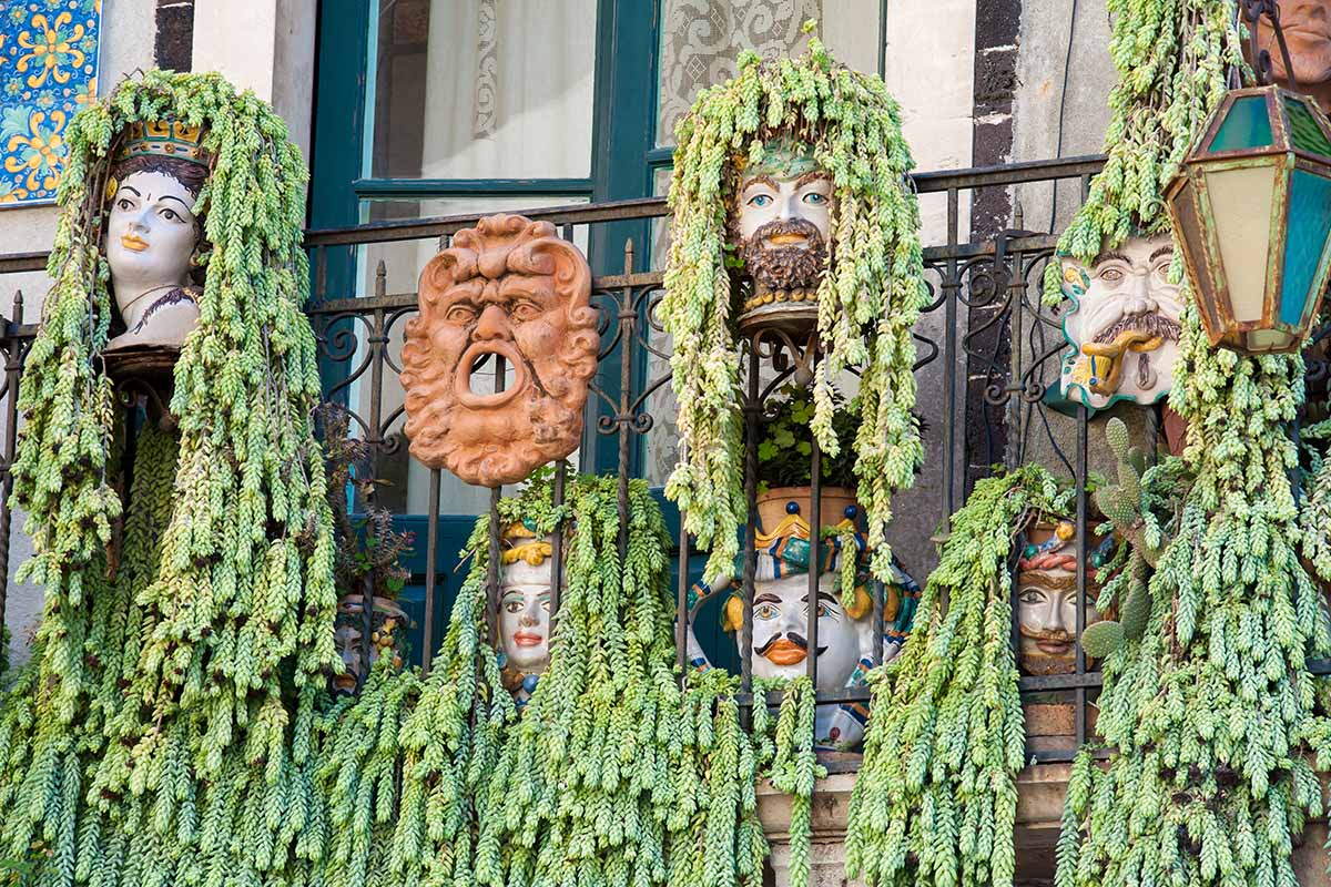 A horizontal image of decorative planters in the shapes of faces with donkey's tail succulents (Sedum morganianum) cascading over the sides giving the impression of hair.